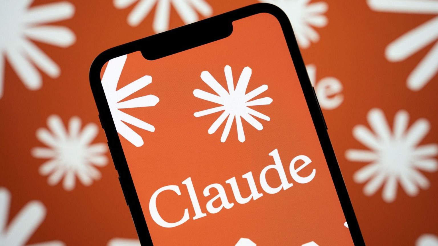 Claude app logo displayed on an iPhone with Anthropic star logo pattern in the background
